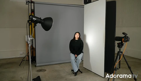 Portrait subject seated in professional studio setup with key light and fill reflectors.
