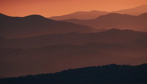 Layered mountain ridges silhouetted against an orange and amber sunset sky.