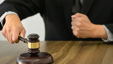 Judge striking a wooden gavel on its sound block during a court proceeding.
