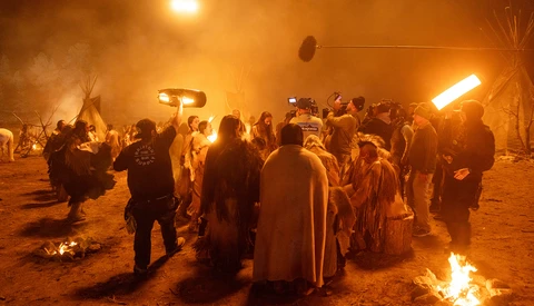 Crowd gathered around fires at night in desert setting with warm orange lighting and smoke.