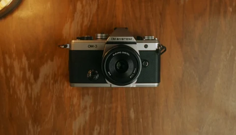 Om System OM-3 rangefinder camera with 38mm lens on wooden surface.