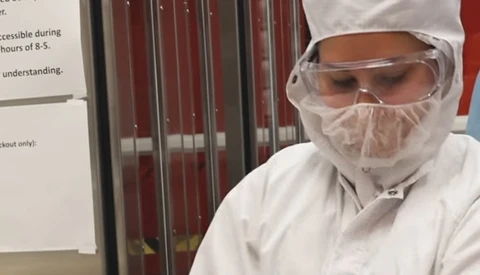 Person wearing full white protective gear including hood, face shield, and goggles in an indoor setting.