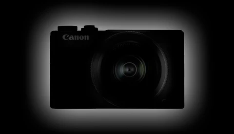 Canon compact digital camera silhouetted against a dark background with rim lighting.