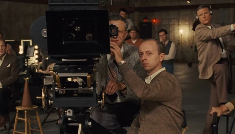 Film director operating a large format movie camera on set with crew members surrounding.