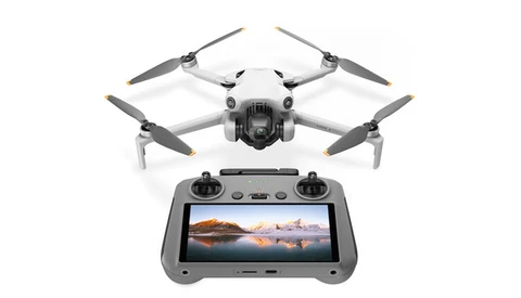 Compact drone with four propellers positioned above its remote controller displaying a landscape photograph on screen.