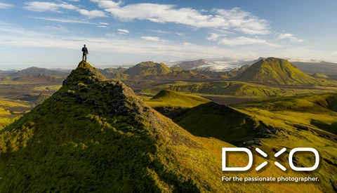 Hiker standing atop a moss-covered peak overlooking an expansive Icelandic landscape with mountains and valleys.