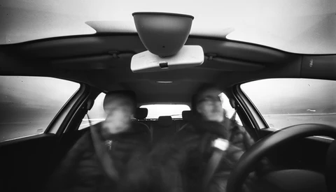 Two blurred figures visible through a car's windshield in black and white.