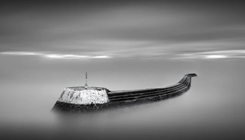 Abandoned wooden boat with snow-covered hull half-submerged in still water.