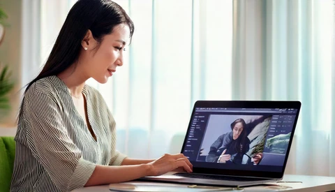 Woman reviewing photo editing software on laptop screen in bright office environment.