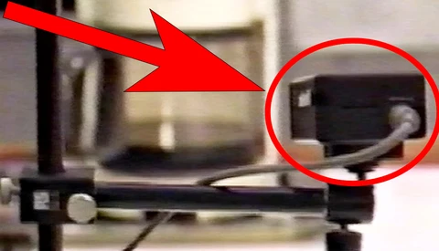 3D printer with red arrow indicating the extruder nozzle and circled detail of the printing head assembly.