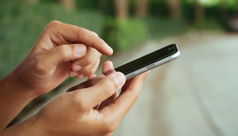 Hands holding a smartphone outdoors with natural daylight illumination.