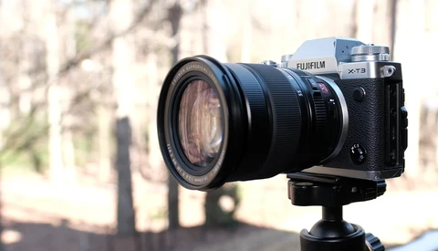 Fujifilm X-T3 camera mounted on tripod with telephoto lens attached, positioned outdoors with blurred architectural background.