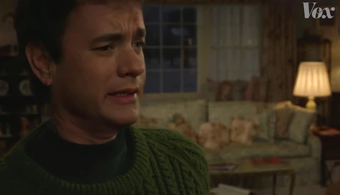 Screenshot from a film showing a man in a green sweater in a warmly lit living room interior.