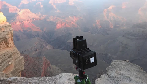 Medium format camera mounted on tripod at Grand Canyon's edge during golden hour sunrise.