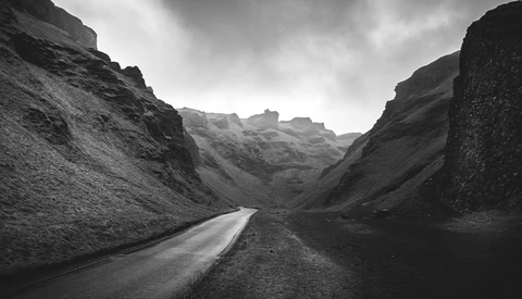 Narrow asphalt road cutting through a volcanic canyon with steep dark rock walls under an overcast sky.