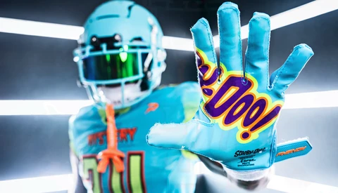 Football player in bright blue uniform extending hand toward camera, wearing colorful receiver gloves with purple and gold design.