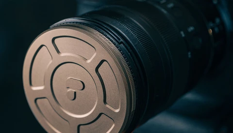 Close-up of a metallic lens cap with circular venting slots and center post, mounted on a camera lens barrel.