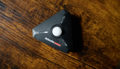 Black triangular camera accessory with white circular button on wooden surface.