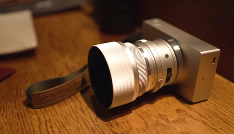 Compact camera with telephoto lens and wrist strap on wooden surface.