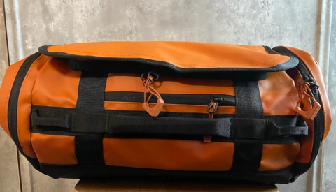 Orange and black cylindrical duffel bag with compression straps, displayed on a concrete surface.