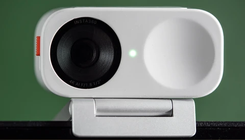 White compact camera with black lens and white viewfinder dome mounted on articulating stand.