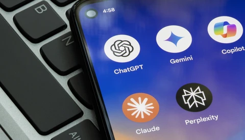 Screenshot showing AI assistant app icons including ChatGPT, Gemini, Copilot, Claude, and Perplexity on a smartphone screen next to a laptop keyboard.