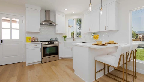 Bright, modern white kitchen with wood flooring, stainless steel appliances, and an island with seating.