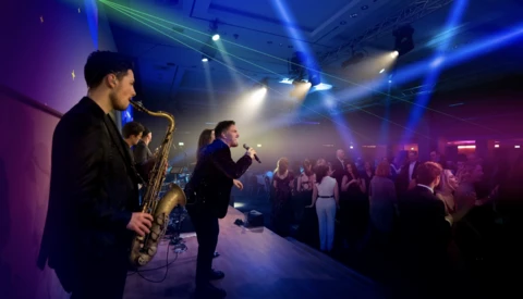 Saxophonist and vocalist performing on stage with dynamic blue and purple lighting during an indoor event.
