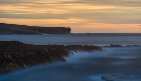 Coastal cliffs and rocky shoreline at twilight with long exposure blur on calm sea.