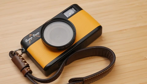 Yellow and black compact camera with built-in flash and brown leather strap on wooden surface.
