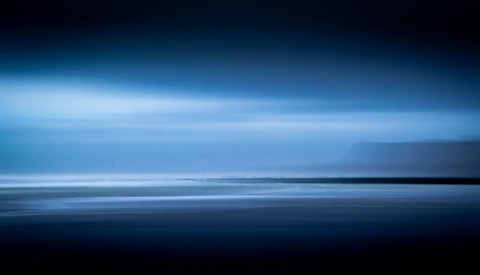 Minimalist seascape with horizontal bands of dark water, light blue sky, and thin luminous line dividing the composition.