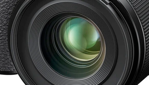 Close-up of a camera lens front element with multi-coated glass and internal lens groups visible.