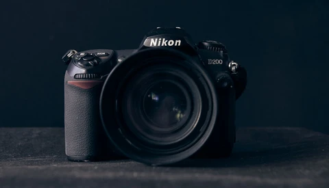 Nikon D200 DSLR camera with attached lens, positioned against a dark background.