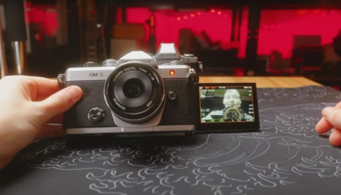 Hands holding a compact rangefinder camera with articulating rear screen displaying a portrait.