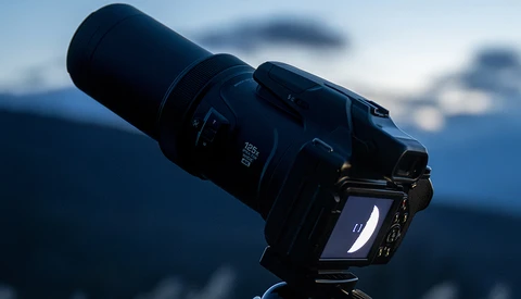 Professional DSLR camera with telephoto lens mounted on tripod against blurred mountain landscape.