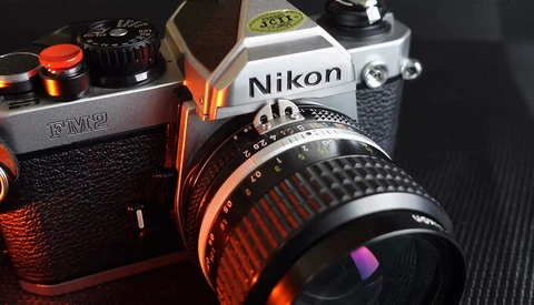Two vintage film SLR cameras with manual focus lenses displayed on dark textured surface with warm orange lighting.