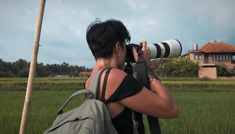 Photographer with telephoto lens shooting in rice paddy landscape with colonial building in background.