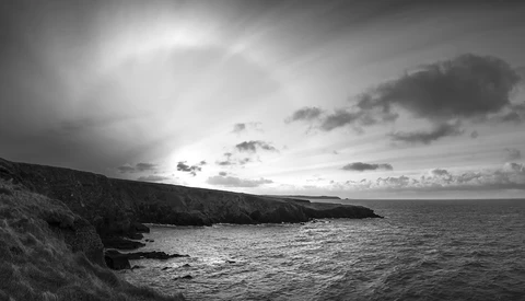 Dramatic black and white coastal landscape with rocky cliffs overlooking turbulent sea under stormy sky.