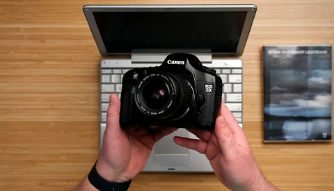Canon EOS 5D Mark IV DSLR camera held above a laptop keyboard on a wooden desk.