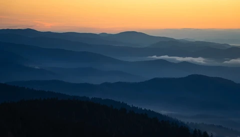 Layered mountain ridges receding into hazy distance under golden sunrise sky.