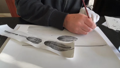 Hand holding pen over printed sketches of elongated organic forms arranged on white paper.