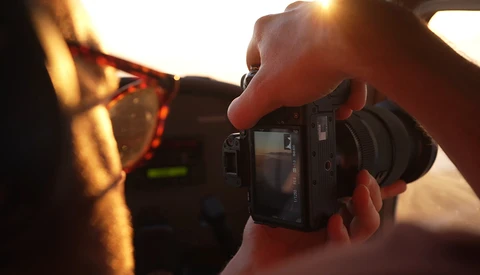 Photographer holding a compact camera while shooting golden hour sunlight through eyeglasses.