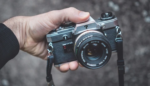 Hand holding a vintage rangefinder camera with leather body and attached neck strap.