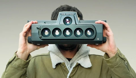 Photographer holding a panoramic film camera with six lenses across its front.