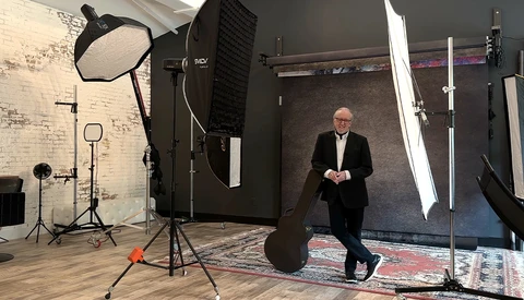 Man in business attire standing in a professional photography studio with softbox lighting and reflector equipment.