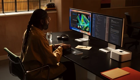 Creative professional working at a dual-monitor setup with colorful data visualization displayed on screen.