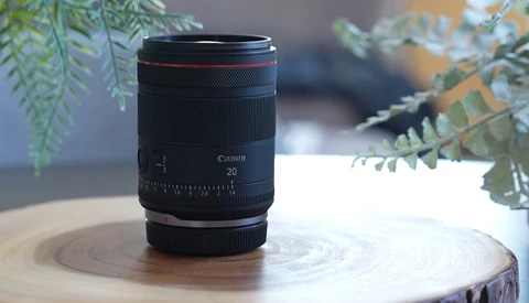 Canon RF 20mm lens displayed on a wooden surface with green foliage in the background.