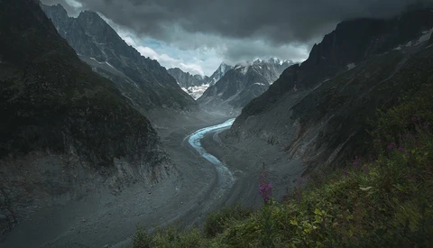 Winding river cuts through a dramatic mountain valley beneath storm clouds.