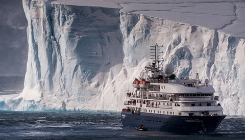 Expedition ship navigating alongside towering white ice cliffs in polar waters.
