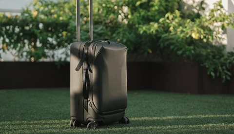 Black hardside rolling suitcase with extended handle standing on grass outdoors.